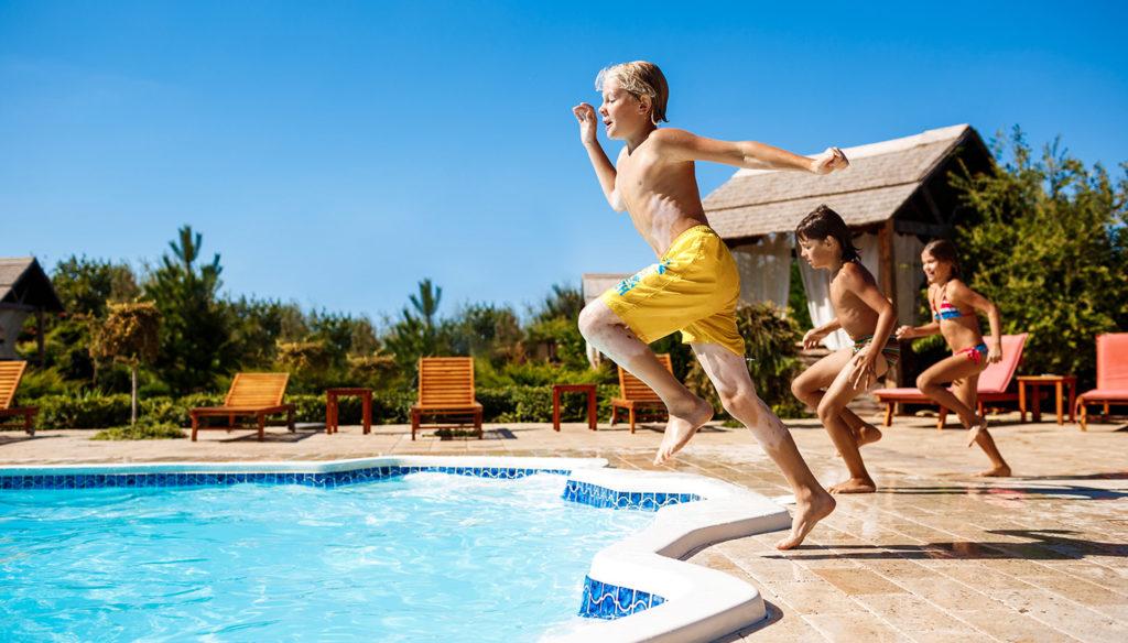 Cheerful children rejoicing, jumping, swimming in pool.